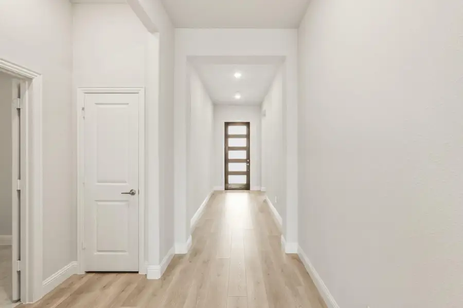 Hallway with white walls, light wood floors, and dark wood front door with glass panels Hallway with white walls, light wood floors, and dark wood front door with glass panels