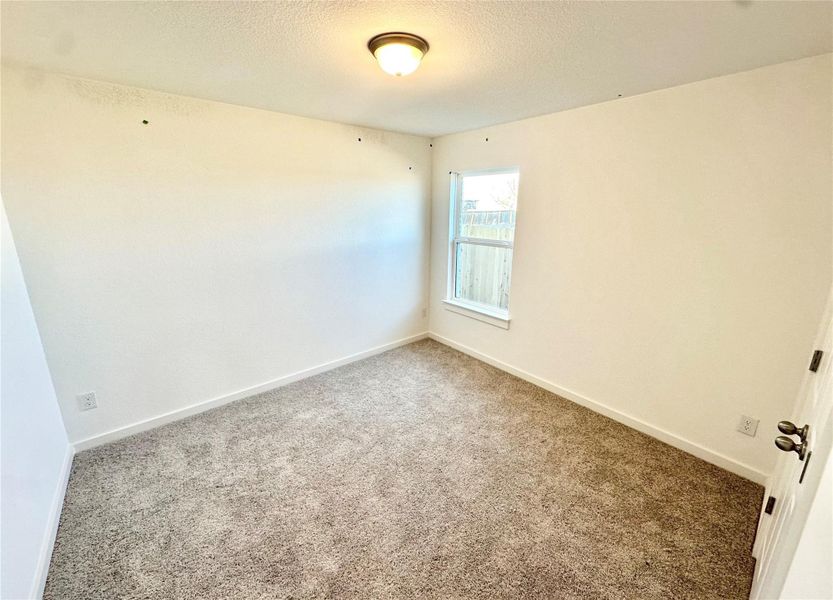 Carpeted spare room featuring a textured ceiling and baseboards