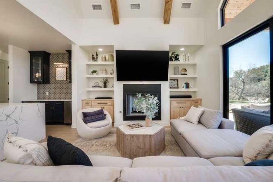 Living area featuring a fireplace, light wood-style floors, beamed ceiling, and a high ceiling