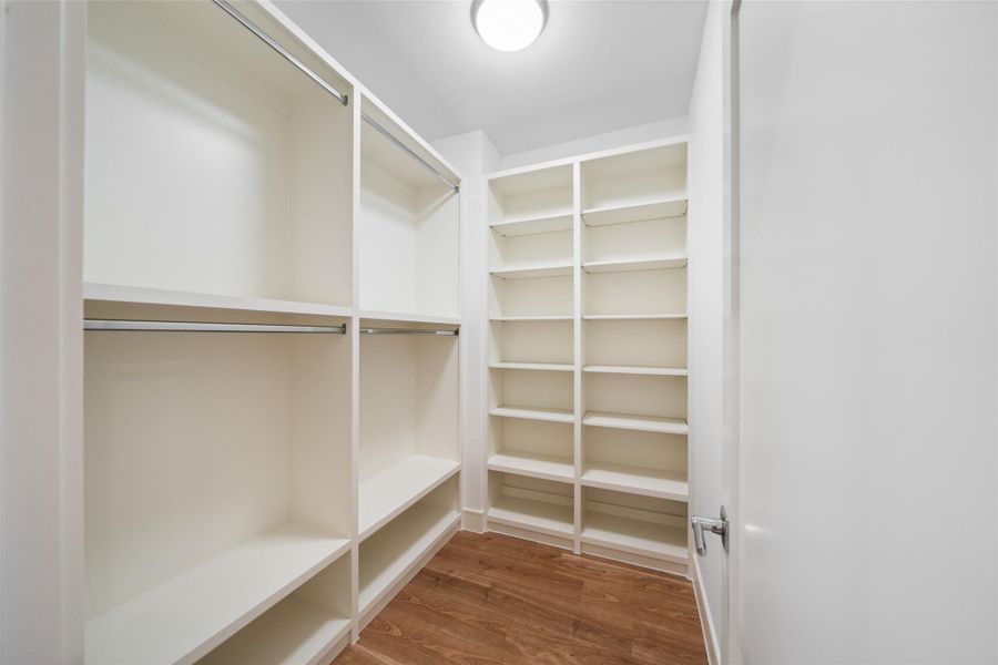 Spacious walk-in closet with ample shelving and hanging space, featuring a clean, modern design and wood flooring.