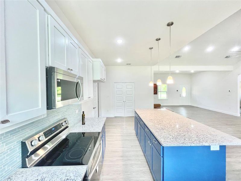 Kitchen featuring blue cabinetry, light stone counters, stainless steel appliances, light wood finished floors, and decorative backsplash