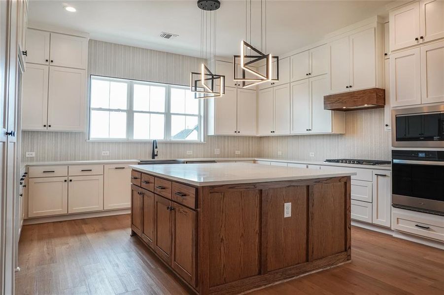 Kitchen featuring stainless steel appliances, a kitchen island, light wood-type flooring, pendant lighting, and white cabinets