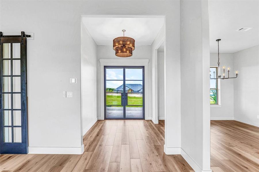 Entrance foyer featuring a barn door, light wood-type flooring, french doors, and an inviting chandelier