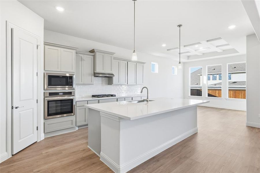 Kitchen with coffered ceiling, gray cabinetry, appliances with stainless steel finishes, light wood-style flooring, and hanging light fixtures Kitchen with coffered ceiling, gray cabinetry, appliances with stainless steel finishes, light wood-style flooring, and hanging light fixtures
