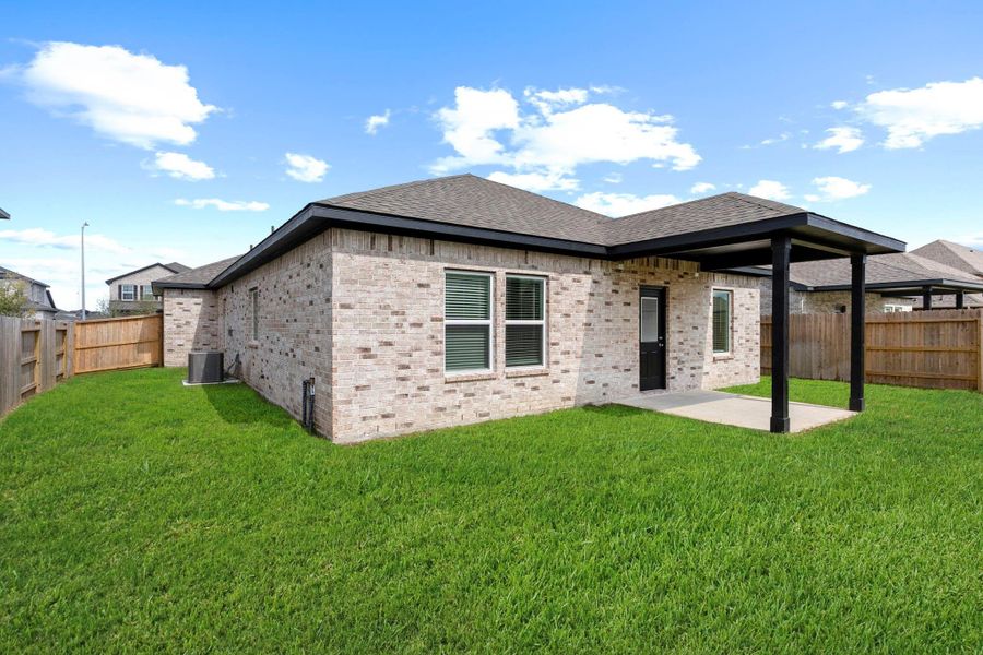 Rear view of the home showcasing the covered patio and elegant brick exterior. The open yard provides endless possibilities for outdoor fun and customization — from a play area to your dream garden setup.