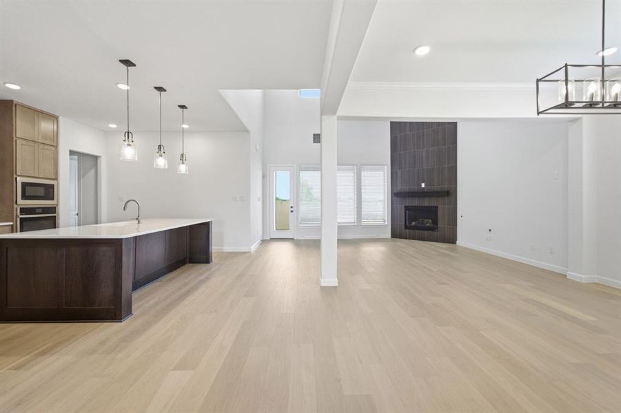 Spacious interior featuring light wood-finish flooring, a kitchen island with pendant lighting, a tile-accented fireplace, numerous windows, and high ceilings