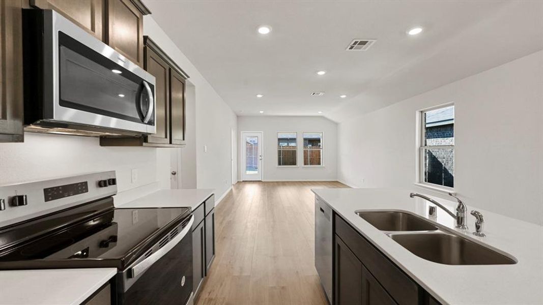 Kitchen with stainless steel appliances, recessed lighting, light wood-type flooring, light stone countertops, and dark wood finish cabinets