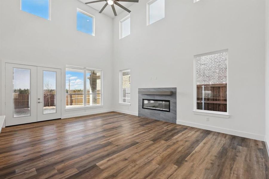 Unfurnished living room with ceiling fan, a fireplace, baseboards, french doors, and dark wood finished floors