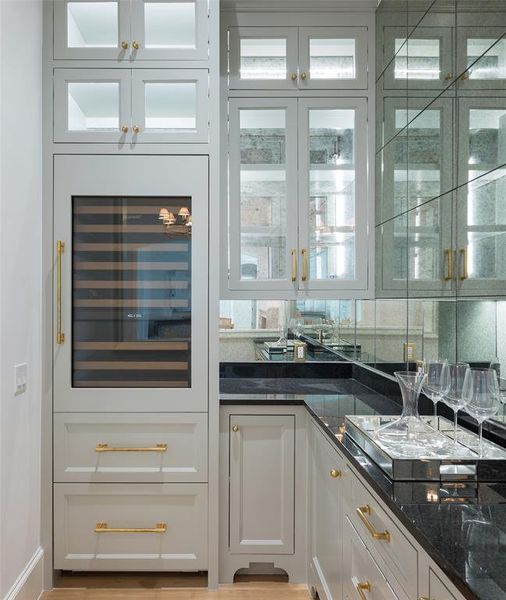 Bar with light hardwood / wood-style floors, dark stone counters, and white cabinetry