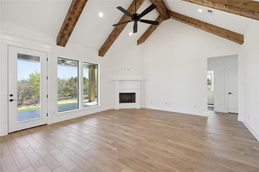 Unfurnished living room featuring beamed ceiling, light wood-type flooring, ceiling fan, and high vaulted ceiling