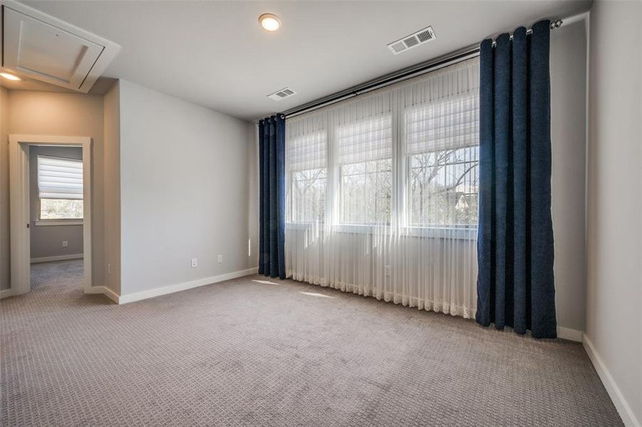 Carpeted empty room featuring attic access, baseboards, and visible vents