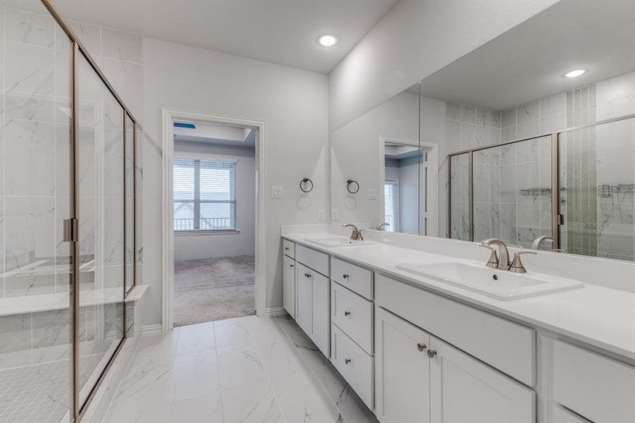 Bathroom featuring a shower stall, double vanity, marble finish floor, and a sink