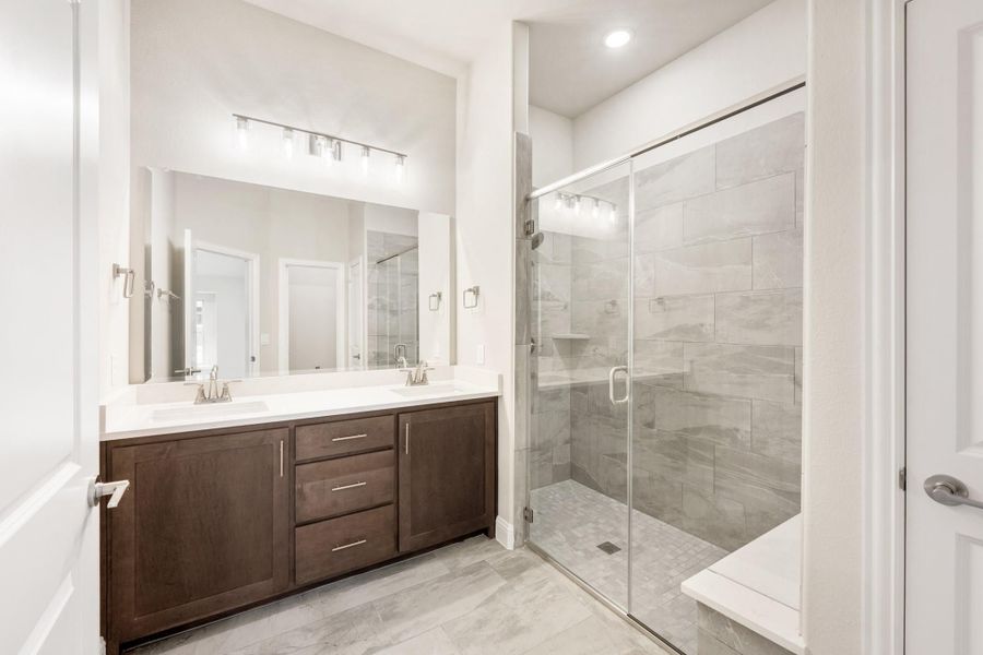Bathroom with double sink vanity, dark wood cabinets, and glass-enclosed tile shower