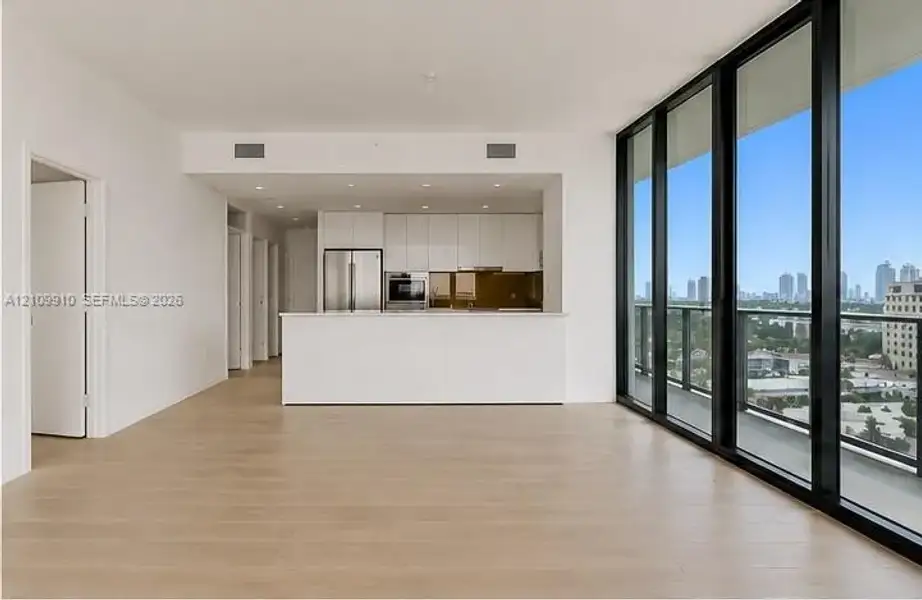 Open-concept interior featuring floor-to-ceiling glass panel walls, wood-finish flooring, white flat-panel cabinetry, stainless steel appliances, and a built-in kitchen peninsula