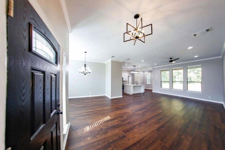 Unfurnished living room with ornamental molding, a chandelier, dark wood-style flooring, a ceiling fan, and recessed lighting Unfurnished living room with ornamental molding, a chandelier, dark wood-style flooring, a ceiling fan, and recessed lighting
