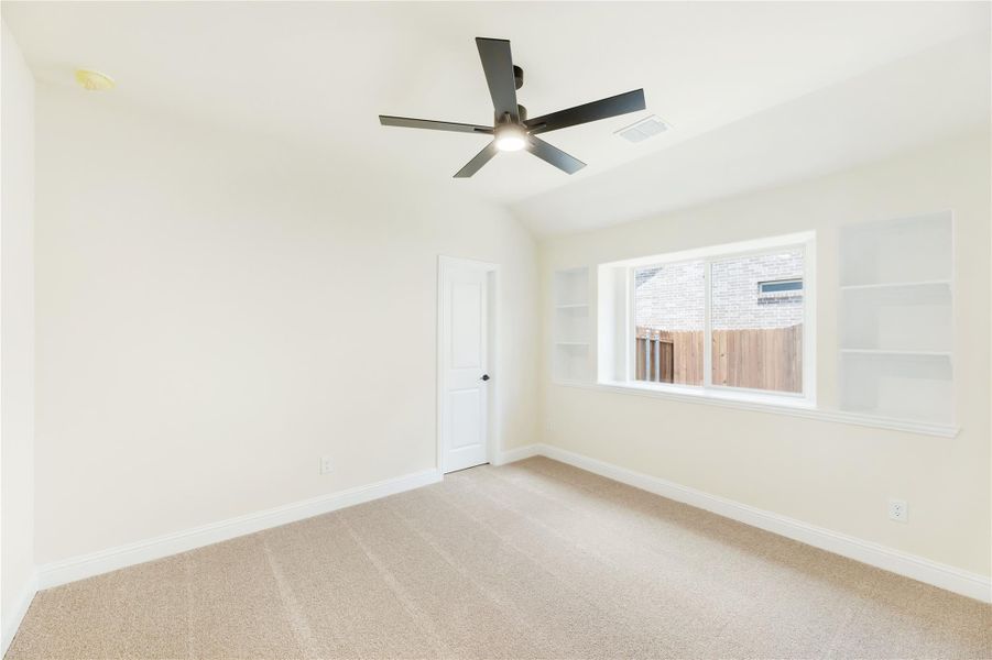 Empty bedroom with vaulted ceiling, ceiling fan, carpet flooring, and built-in shelves beside a window Empty bedroom with vaulted ceiling, ceiling fan, carpet flooring, and built-in shelves beside a window