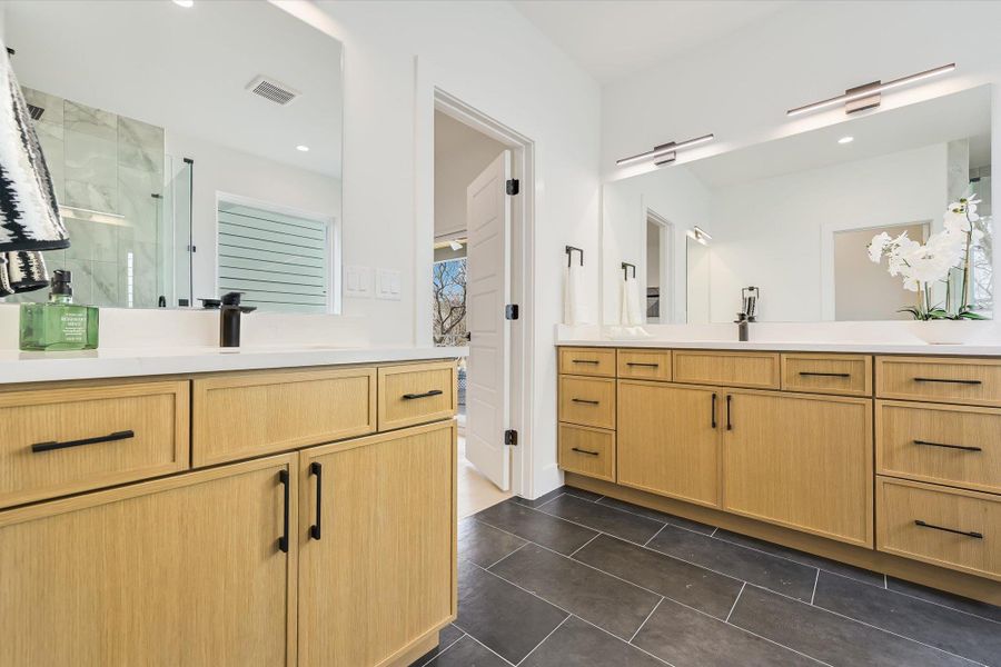 Double the luxury. Dual vanities with natural wood cabinetry and matte black hardware provide a warm, organic contrast to the sleek quartz countertops.