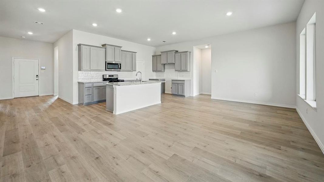 Kitchen featuring gray cabinets, tasteful backsplash, light wood finished floors, appliances with stainless steel finishes, and a kitchen island with sink