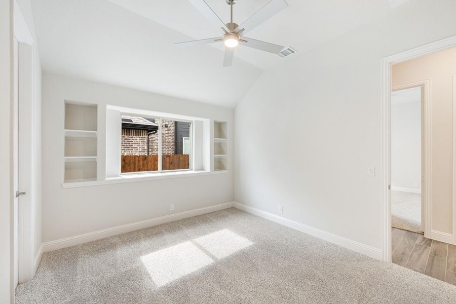 Empty bedroom with vaulted ceiling, ceiling fan, built-in shelves, and carpet flooring