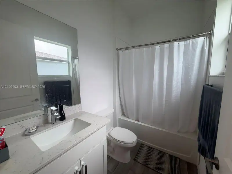 Bathroom featuring a vanity with a light-toned stone countertop, integrated undermount sink, chrome faucet, wall-spanning mirror, and a tub-shower combination with tile surround