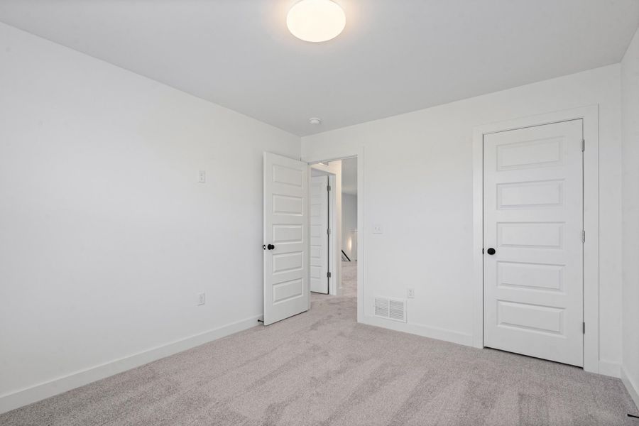 Neutral wall paint with carpet flooring, a flush mount ceiling light, and panel doors with matte black hardware Neutral wall paint with carpet flooring, a flush mount ceiling light, and panel doors with matte black hardware