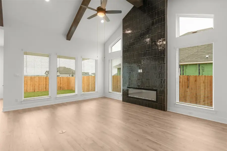 Unfurnished living room with high vaulted ceiling, a fireplace, light wood finished floors, ceiling fan, and beam ceiling Unfurnished living room with high vaulted ceiling, a fireplace, light wood finished floors, ceiling fan, and beam ceiling