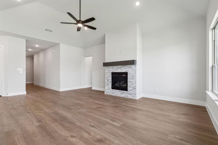 Unfurnished living room with ceiling fan, high vaulted ceiling, light wood-type flooring, and a stone fireplace