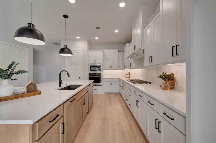 Two tone kitchen featuring two tone cabinets, stainless steel appliances, decorative backsplash, light wood finished floors, and light stone counters