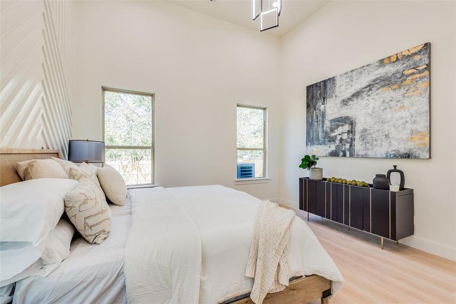 Bedroom with hardwood / wood-style floors, a towering ceiling, and multiple windows