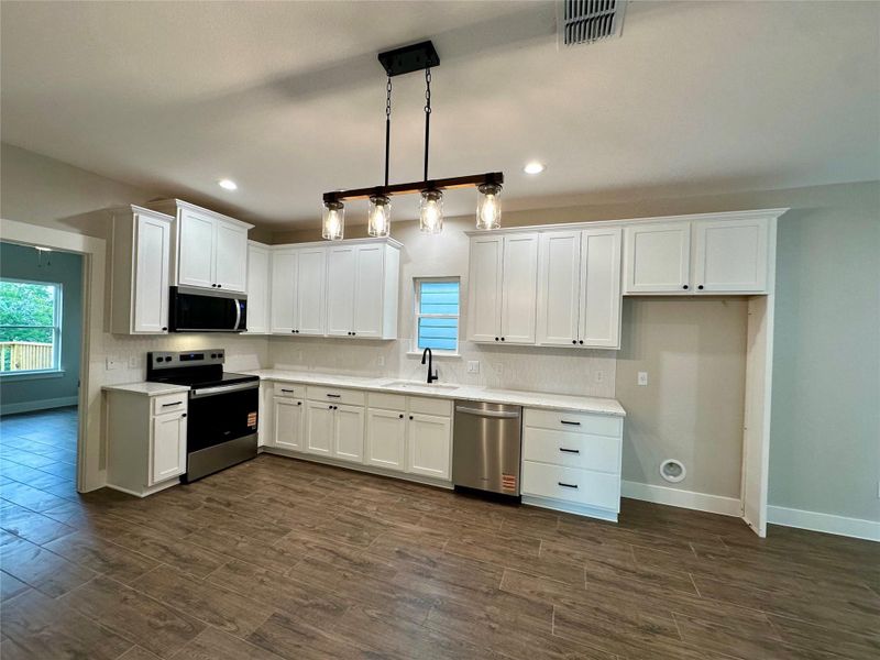 Kitchen with appliances with stainless steel finishes, dark wood-type flooring, white cabinetry, light countertops, and recessed lighting