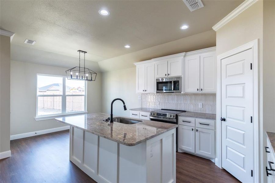 Kitchen featuring a central island with an undermount sink and matte black faucet, granite countertops, white cabinetry, and stainless steel appliances