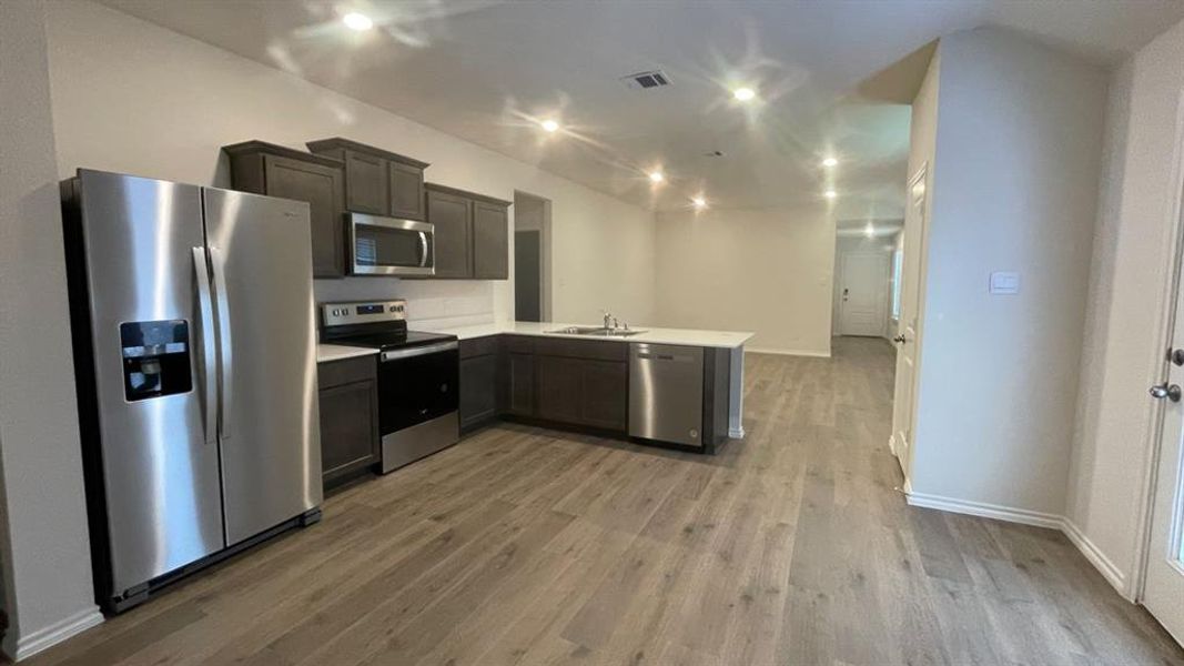 Contemporary kitchen featuring stainless steel appliances, dark wood-finish cabinetry, a large kitchen island with a sink, recessed lighting, and wood-finish flooring Contemporary kitchen featuring stainless steel appliances, dark wood-finish cabinetry, a large kitchen island with a sink, recessed lighting, and wood-finish flooring
