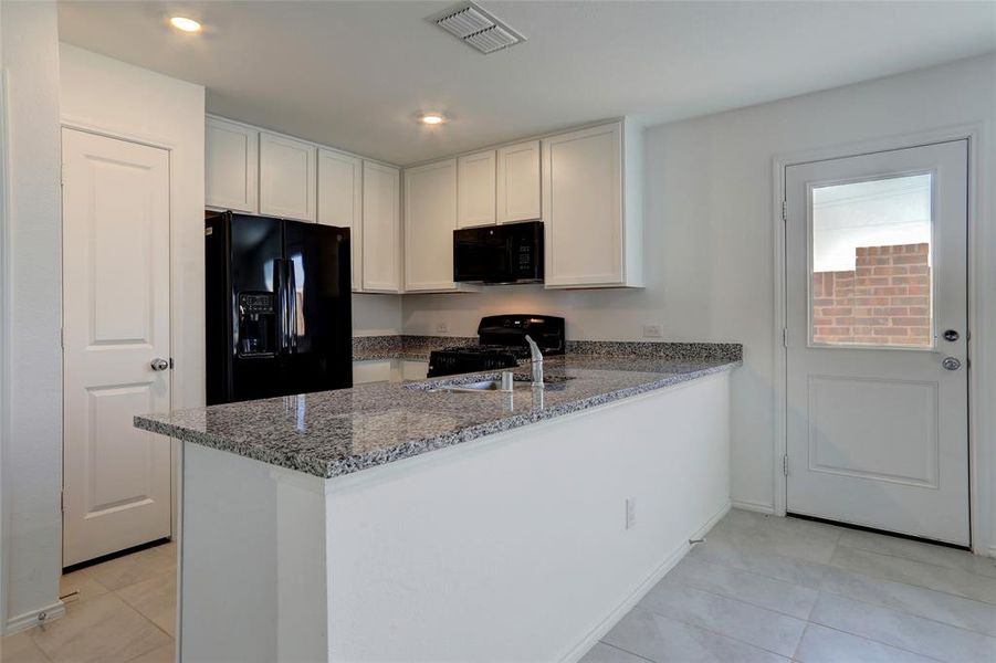 Kitchen featuring black appliances, dark stone counters, light tile patterned floors, white cabinets, and a peninsula