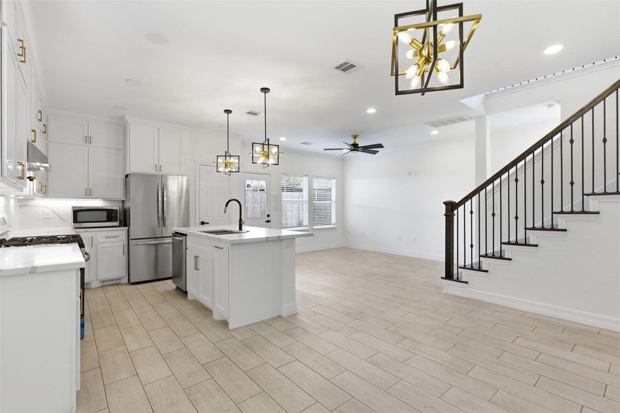 Open concept kitchen and living area with large island, designer pendant lighting, and staircase in the background.