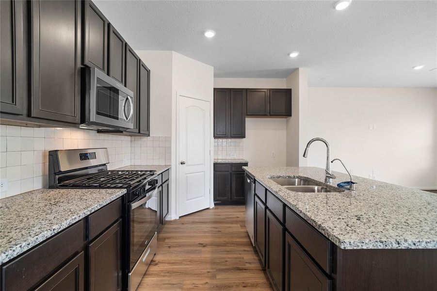 This spacious kitchen features high ceilings, stained wood cabinets, granite countertops, SS appliances, modern tile backsplash, recessed lighting, huge granite kitchen island with large single sink and space for breakfast bar, and a pantry all overlooking your huge family room.