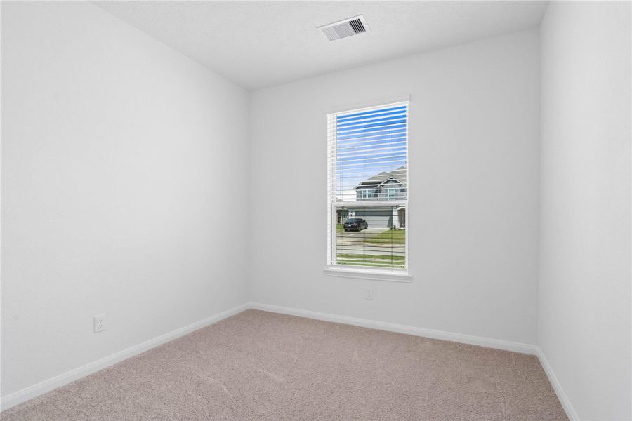 Nestled in the front of the home is this secondary bedroom. It features plush carpet, neutral paint, a large window with privacy blinds, and ample closet space.