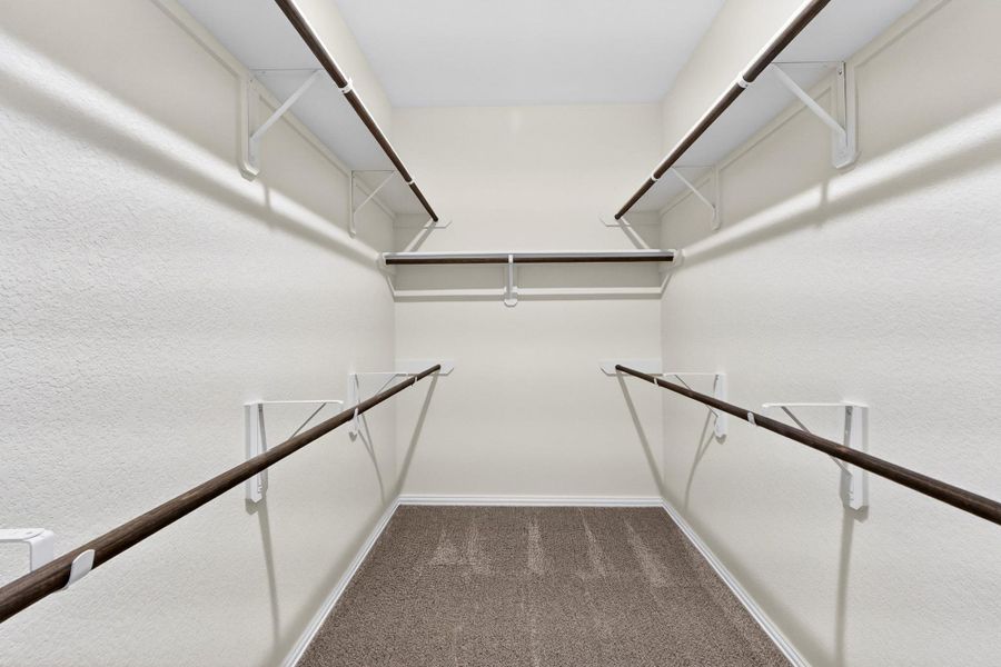 A spacious walk-in closet includes built-in shelving, hanging rods, and carpet flooring.