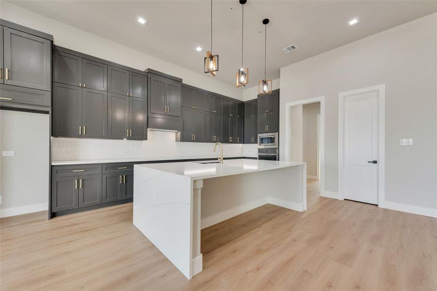 Kitchen featuring backsplash, decorative light fixtures, light hardwood / wood-style floors, a kitchen island with sink, and stainless steel appliances