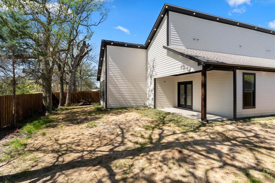 Rear view of house featuring a covered patio area, a fenced backyard, a shingled roof, and french doors