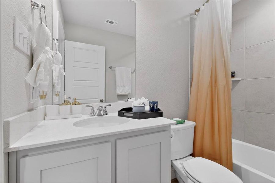 The bathroom features a vanity with a white countertop and a sink, a toilet, and a bathtub with a shower curtain