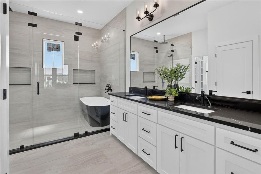 Spacious bathroom featuring a dual vanity with black countertops, white shaker cabinetry, and matte black hardware
