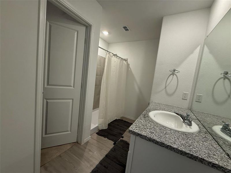 Bathroom featuring a stone-look countertop with an integrated sink, a large wall-mounted mirror, and a tiled shower with a bathtub Bathroom featuring a stone-look countertop with an integrated sink, a large wall-mounted mirror, and a tiled shower with a bathtub