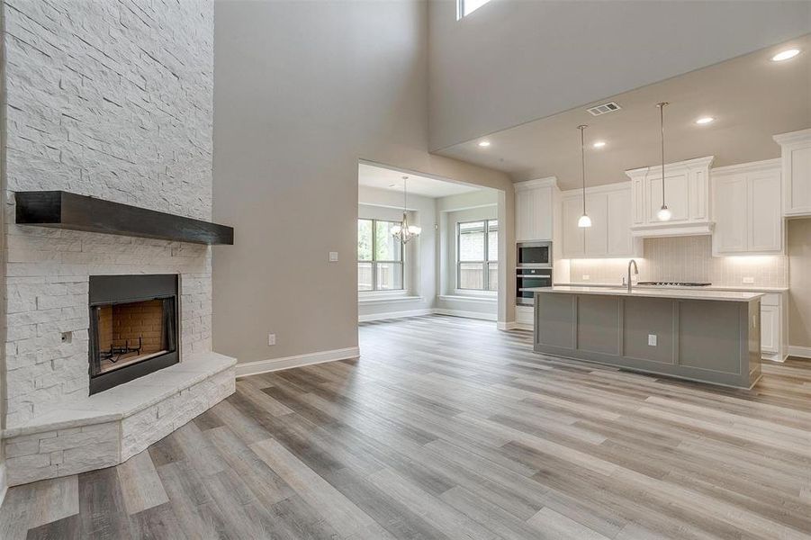 Unfurnished living room with a fireplace, sink, light wood-type flooring, and a high ceiling