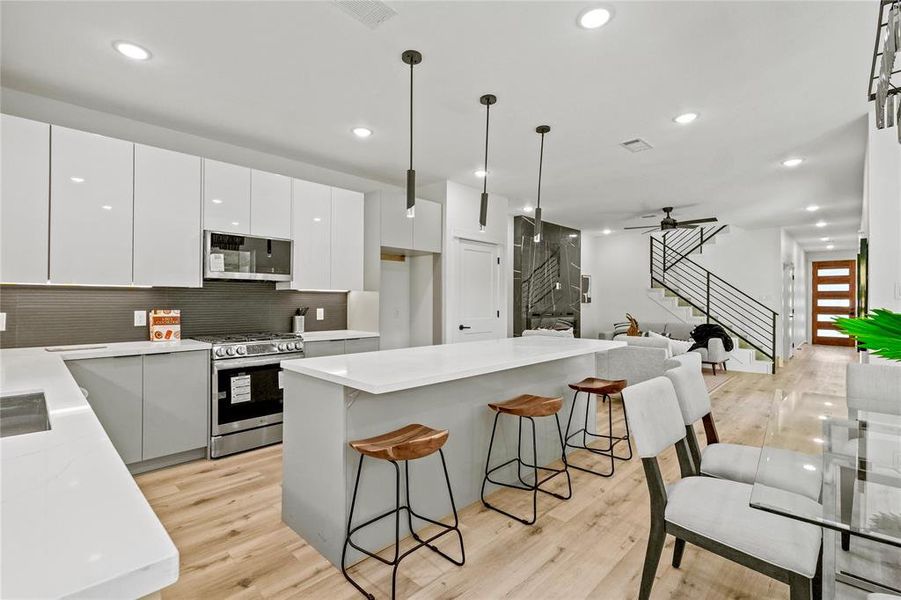 Kitchen featuring stainless steel appliances, light hardwood / wood-style floors, pendant lighting, and white cabinetry