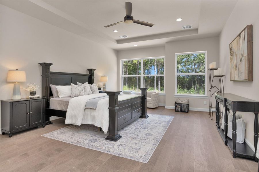 The spacious primary suite offers a peaceful retreat with wood flooring, a tray ceiling and a generous sitting area surrounded by large windows that frame relaxing wooded views.