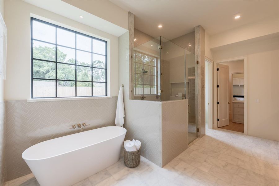 Natural light pours into the serene primary bath, where a matte white Victoria + Albert freestanding tub sits gracefully beneath a large picture window framed in black steel. The surrounding walls are wrapped in a soft herringbone tile, offering texture and subtle sheen. Natural light pours into the serene primary bath, where a matte white Victoria + Albert freestanding tub sits gracefully beneath a large picture window framed in black steel. The surrounding walls are wrapped in a soft herringbone tile, offering texture and subtle sheen.