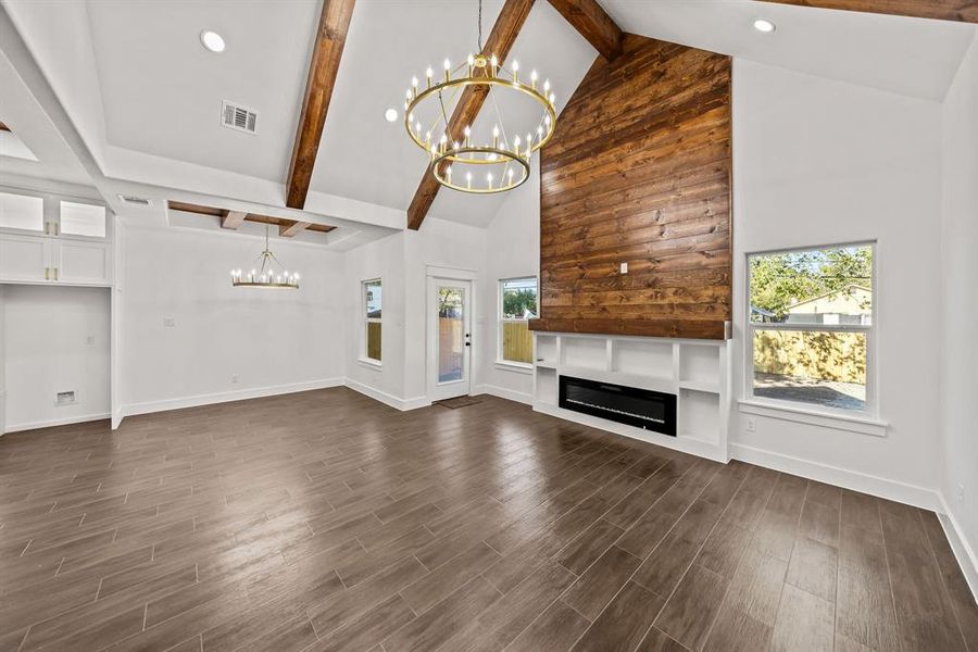 Unfurnished living room with high vaulted ceiling, beamed ceiling, a chandelier, dark wood-type flooring, and a glass covered fireplace Unfurnished living room with high vaulted ceiling, beamed ceiling, a chandelier, dark wood-type flooring, and a glass covered fireplace