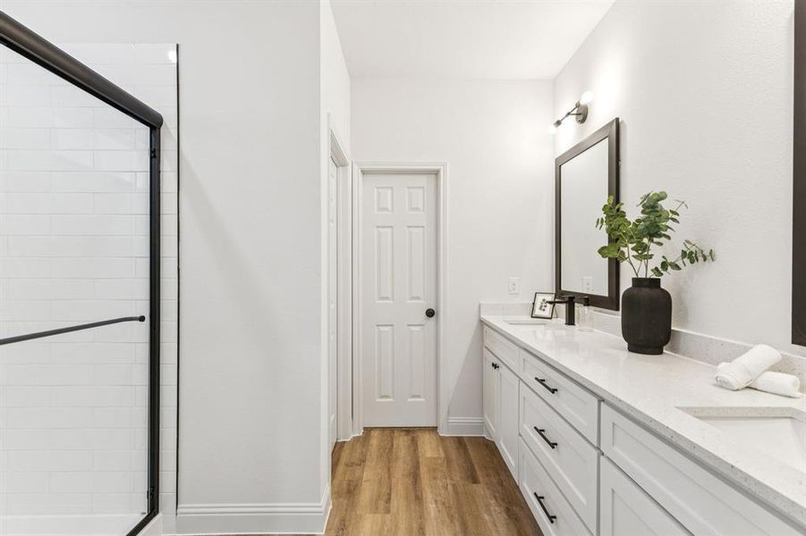 Bathroom featuring a stall shower, double vanity, and light wood-type flooring