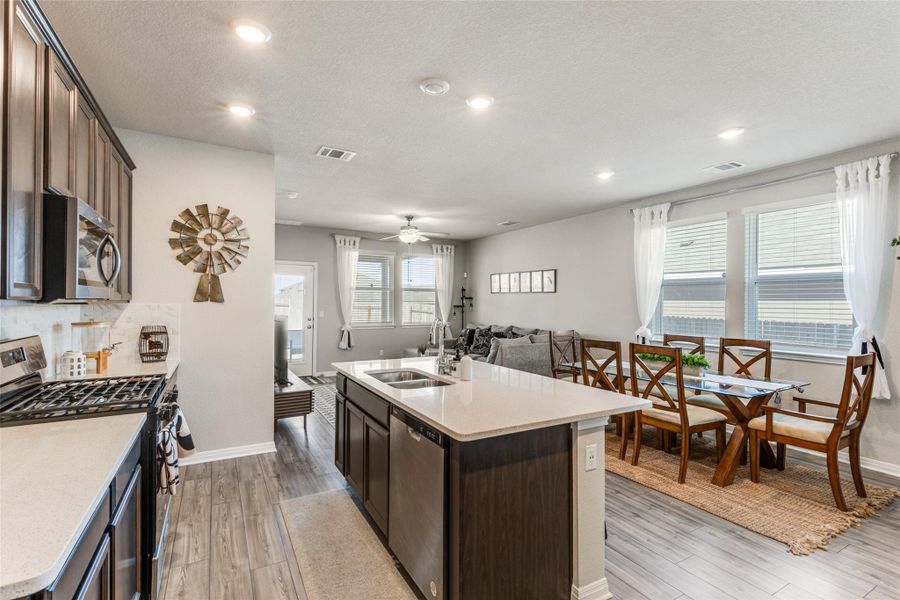 Kitchen with appliances with stainless steel finishes, dark brown cabinetry, a center island with sink, open floor plan, and light wood finished floors