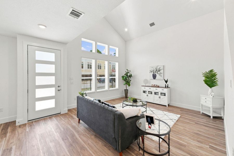 Spacious living room with soaring ceilings, abundant natural light, and a modern front door complemented by multiple windows. Spacious living room with soaring ceilings, abundant natural light, and a modern front door complemented by multiple windows.